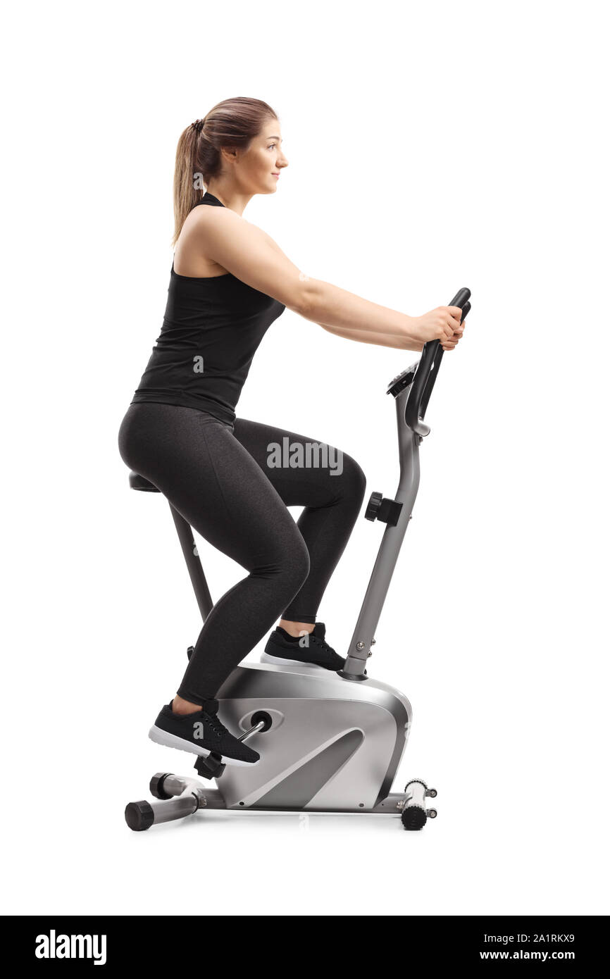 Full length profile shot of a young woman riding a stationary bike isolated on white background Stock Photo