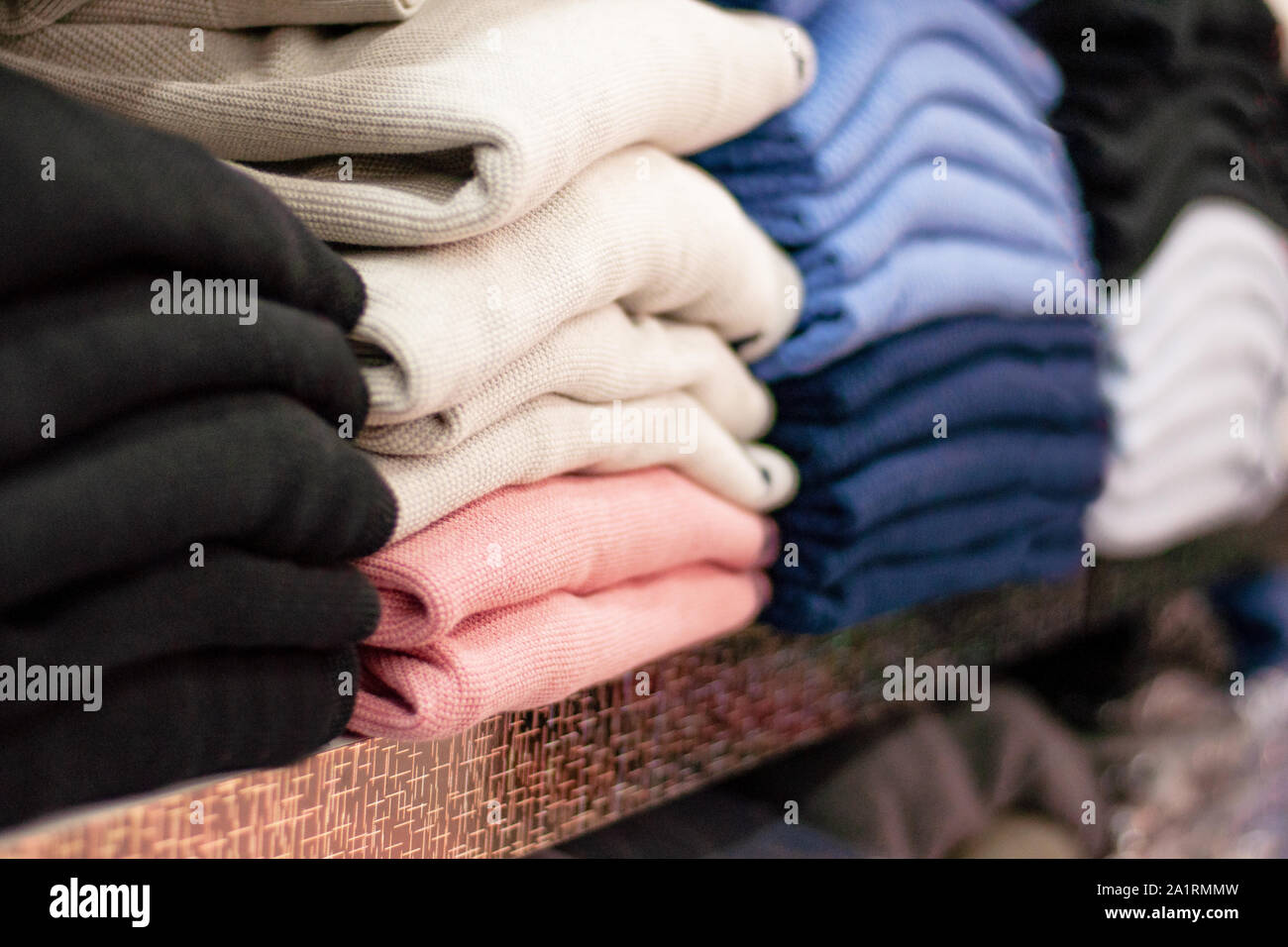 Warm clothing neatly folded on a store shelf. Sweatshirts, sweaters, jumpers, cardigans, hoodies, bobmers with piles on the shelf. Clothes storage. Si Stock Photo