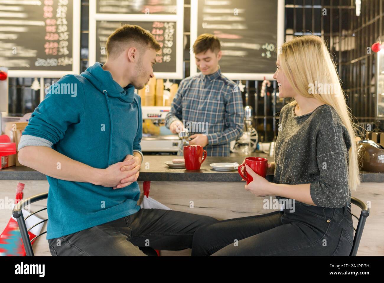 Young smiling man and woman together talking in coffee shop sitting near bar counter, couple of friends drinking tea, coffee Stock Photo