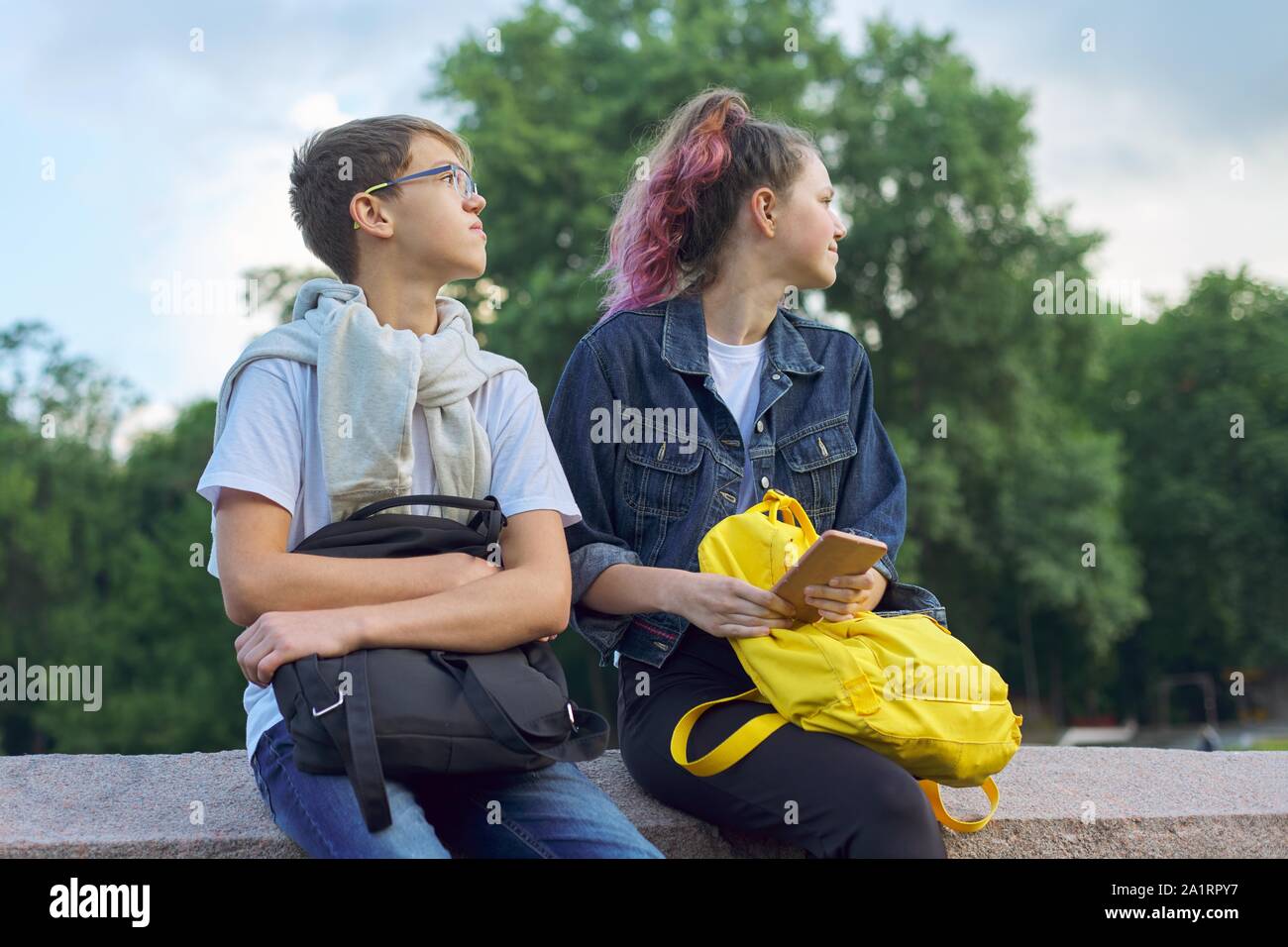 Outdoor portrait of two talking teenagers school students, boy and girl students with smartphone Stock Photo