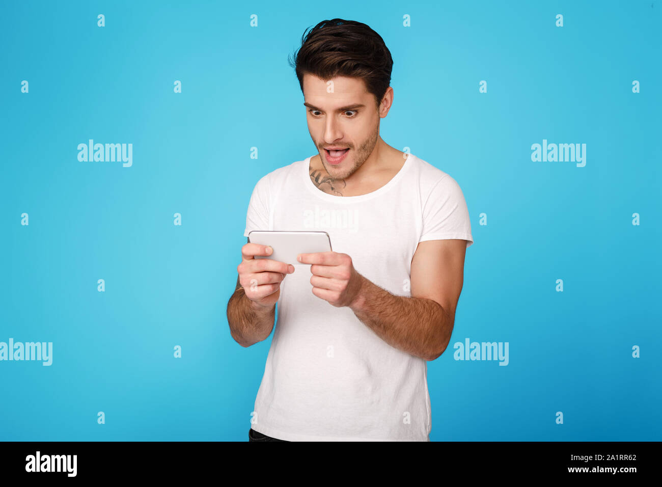 Concentrated young man playing on smartphone, blue background Stock Photo