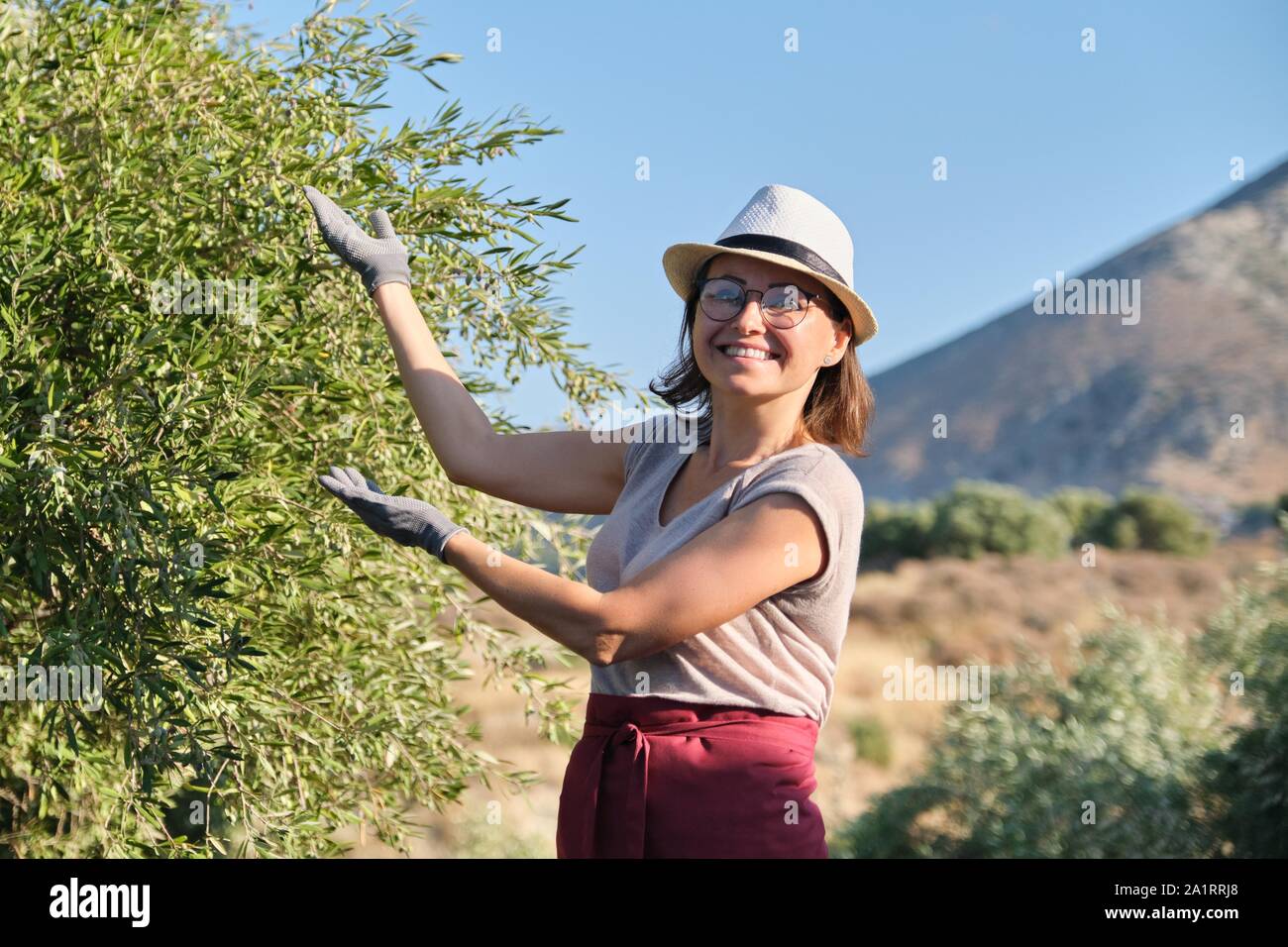 Smiling Woman Owner Of An Olive Garden Pointing To An Tree