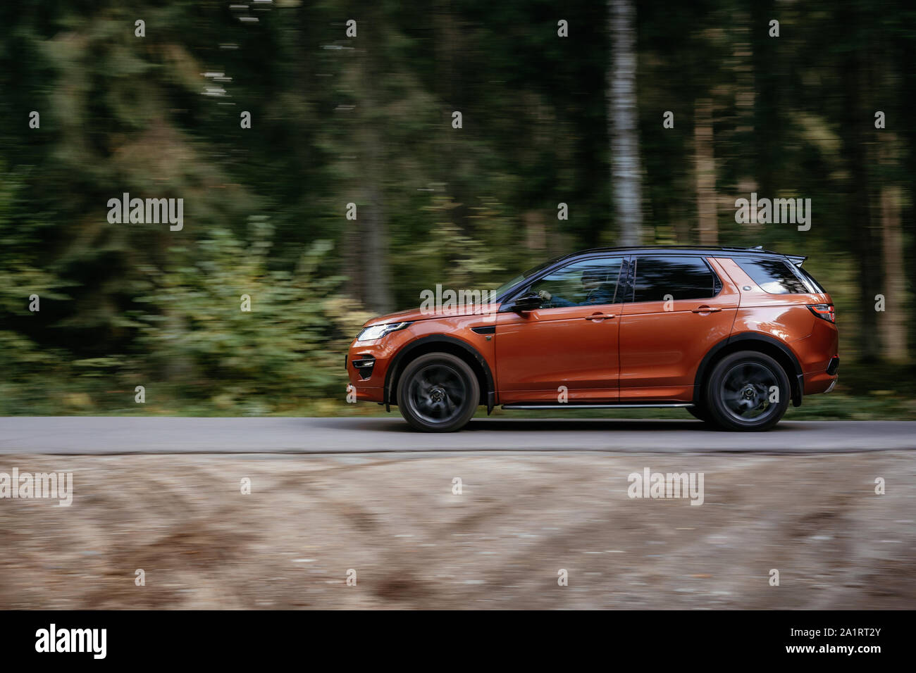 Minsk, Belarus - September 24, 2019: borwn color car Land Rover Discovery Sport fast moving on country road in green autumn forest. Stock Photo