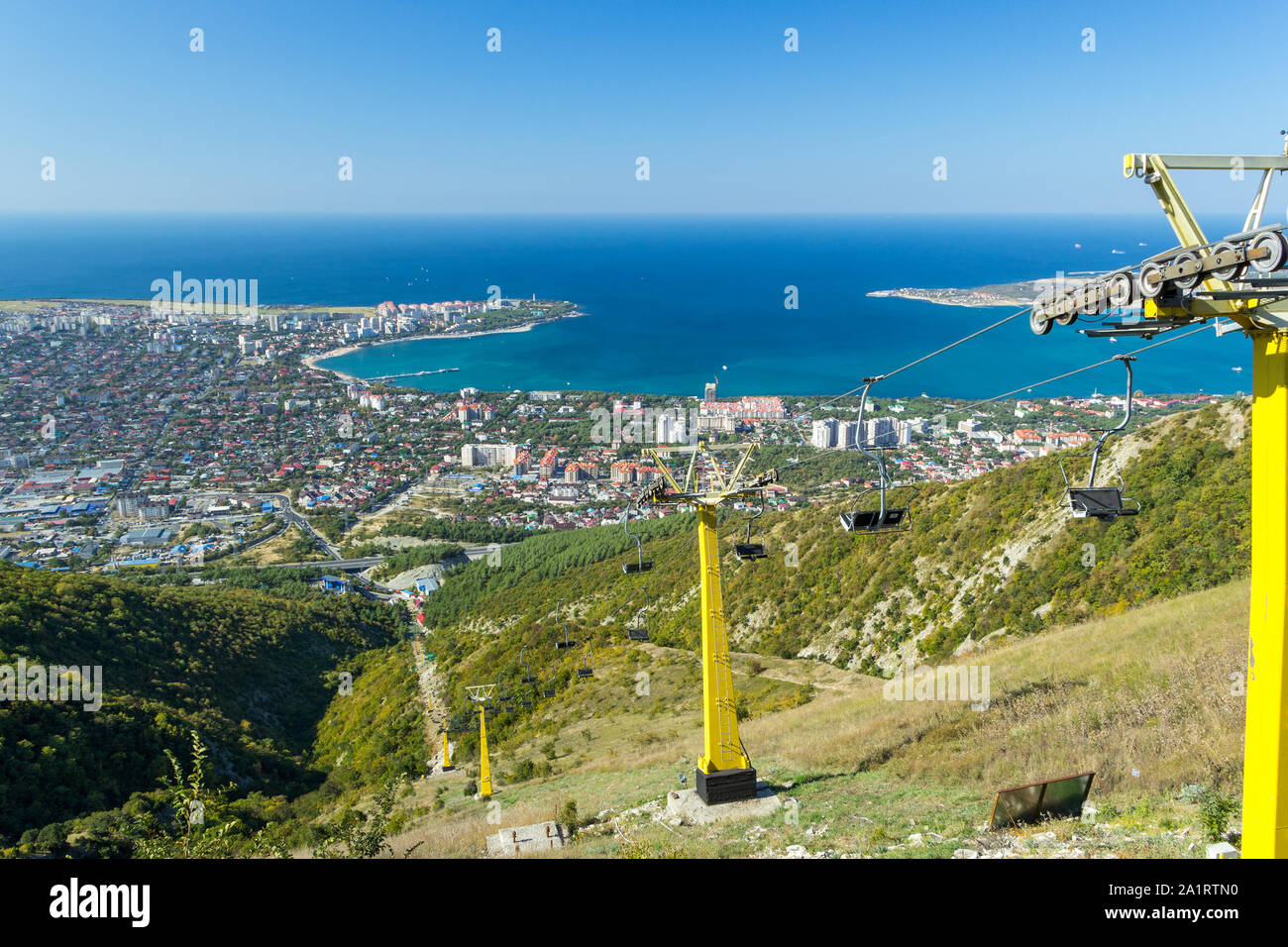 View of chairlift in Caucasus mountains in Gelendzhik resort city with sea bay and Black sea shore in background. Sunny day. Stock Photo