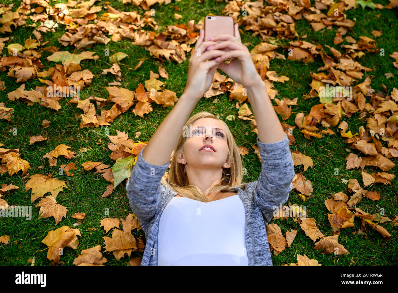 Young woman lying on her back in the grass and the fallen brown leaves ...