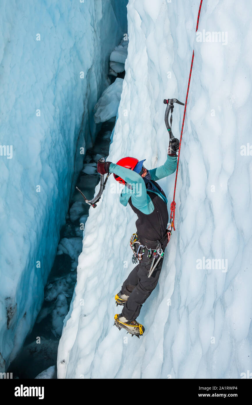 Female ice climber swinging ice tool inside a water filled crevasse on