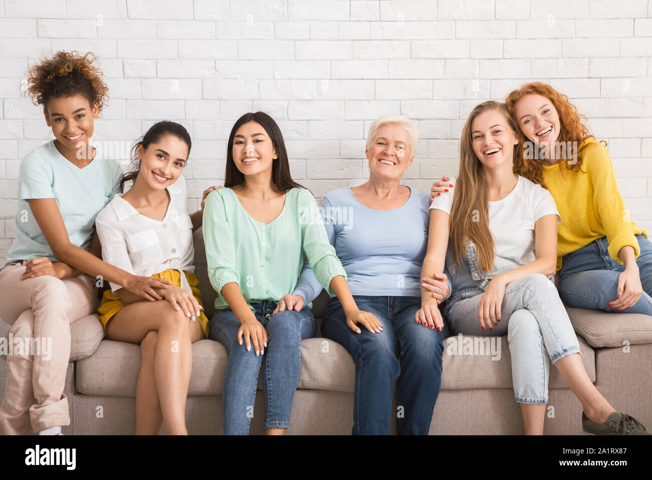 Group Of Women Smiling Sitting On Couch Against White Wall Stock Photo