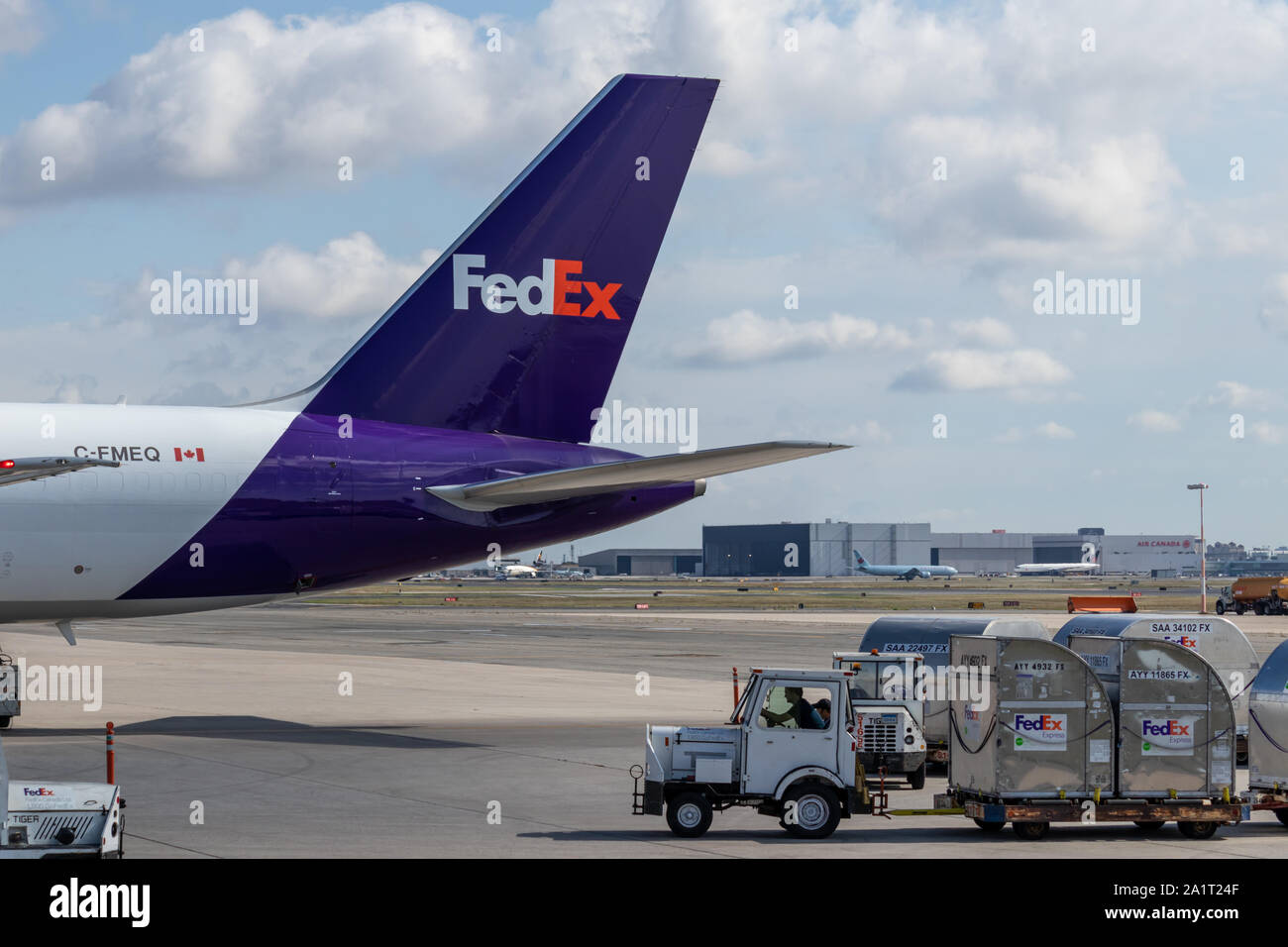 Tail of FedEx cargo plane as man drives tug with cargo containers attached at Toronto Pearson Intl. Airport. Stock Photo