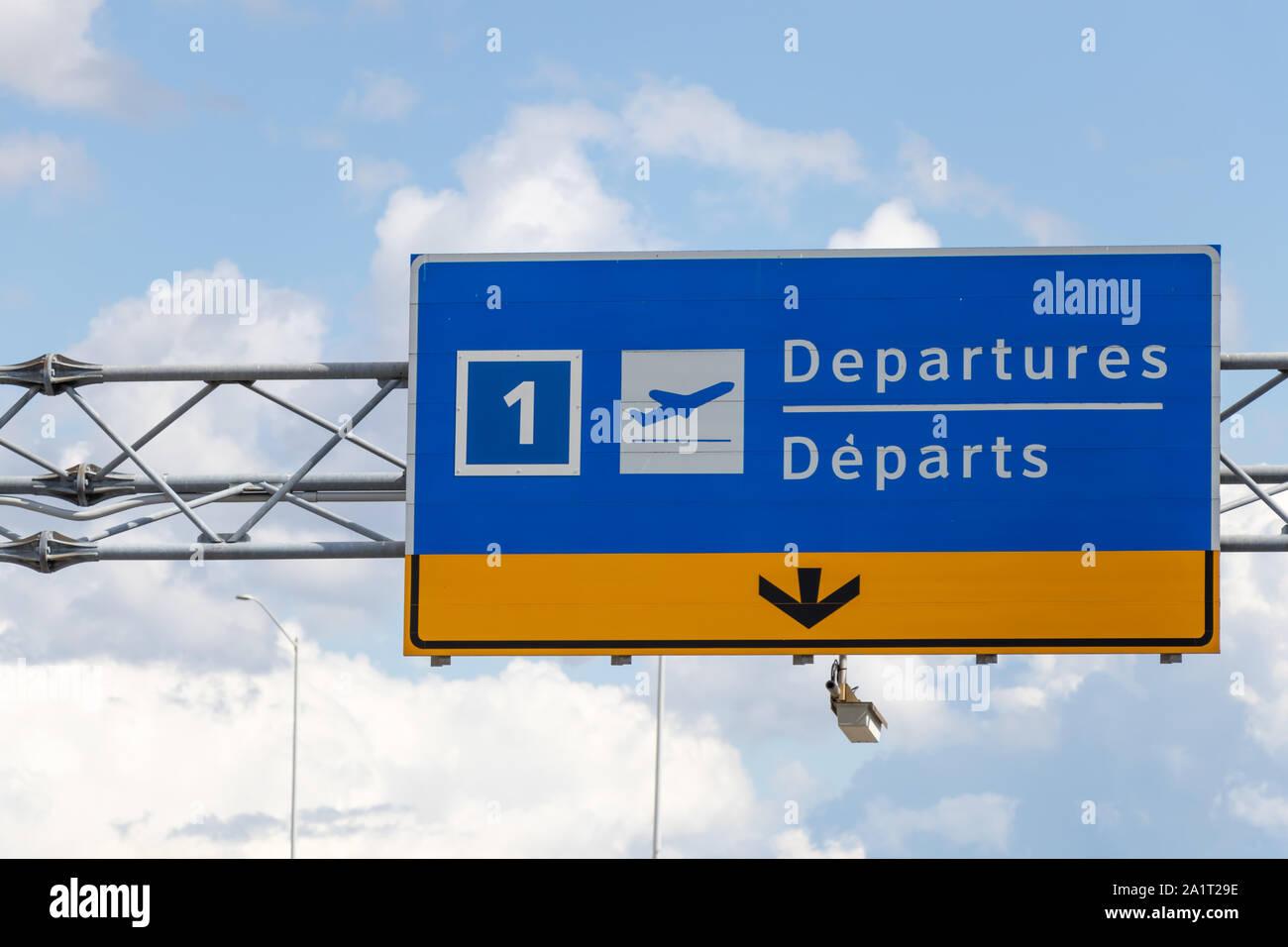 Airport Departures (English/French) sign above roadway on partly cloudy day. Stock Photo