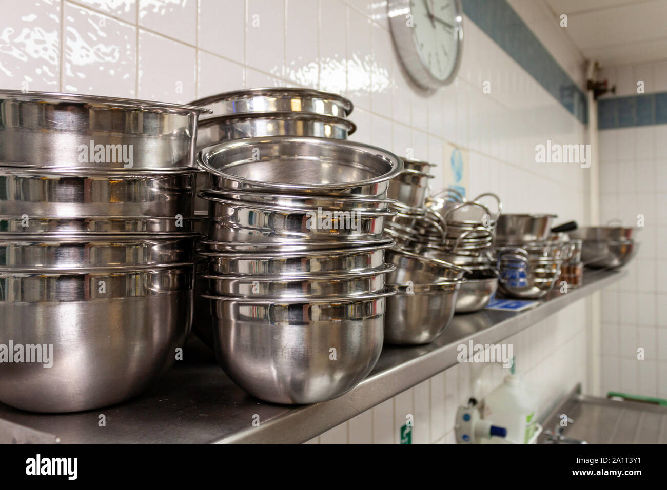 Stainless steel mixing bowls on a stainless steel shelf in an industrial kitchen Stock Photo