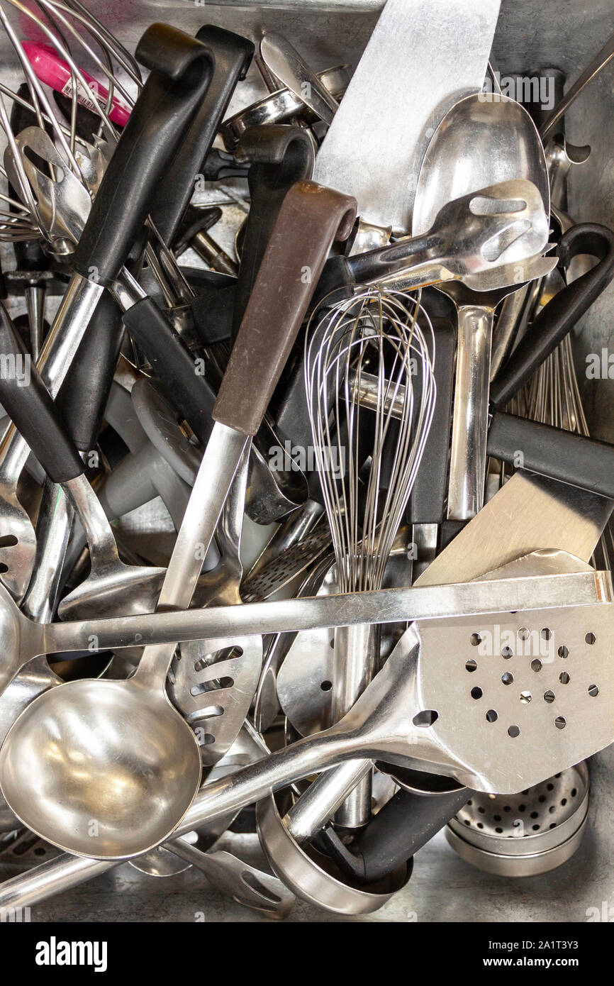Tray of various old stainless steel kitchen cooking utensils in an industrial kitchen Stock Photo