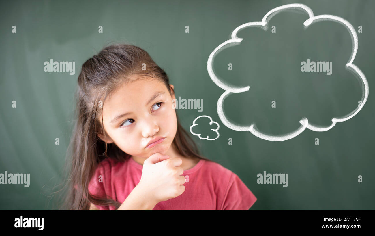 little girl standing against chalkboard with thinking bubble Stock Photo