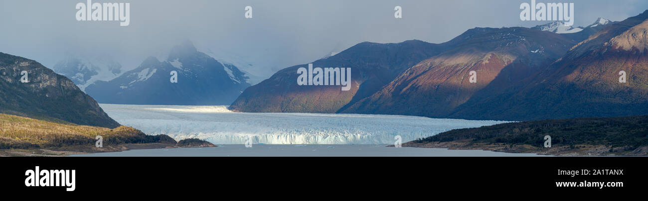 panoramic view of Perito Moreno Glaciar in Argentina. Misty weather in the background, fiultered light on the surrounding moiuntains. Stock Photo