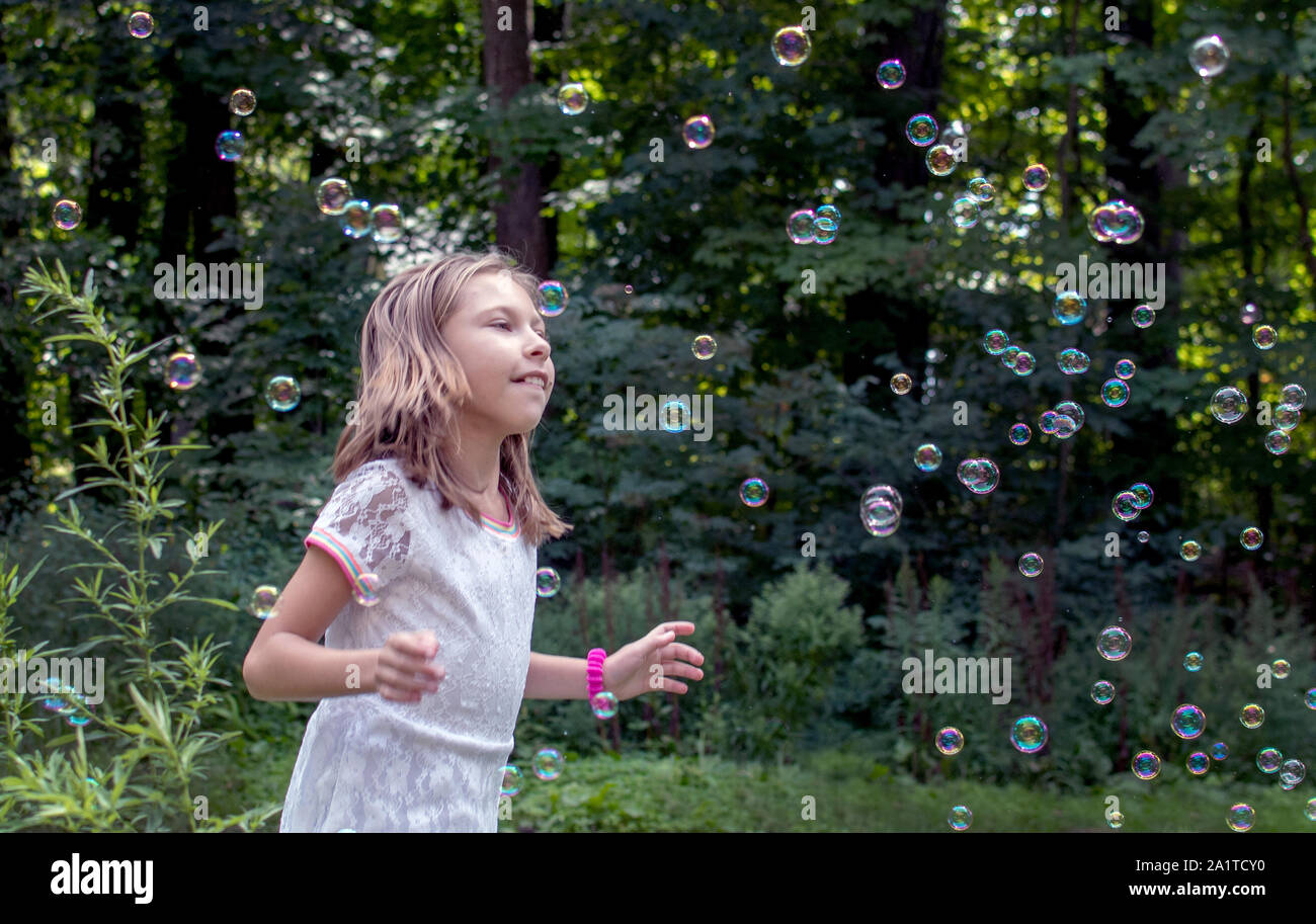 little girl playing outside with bubbles, chasing them as they float through the sky Stock Photo