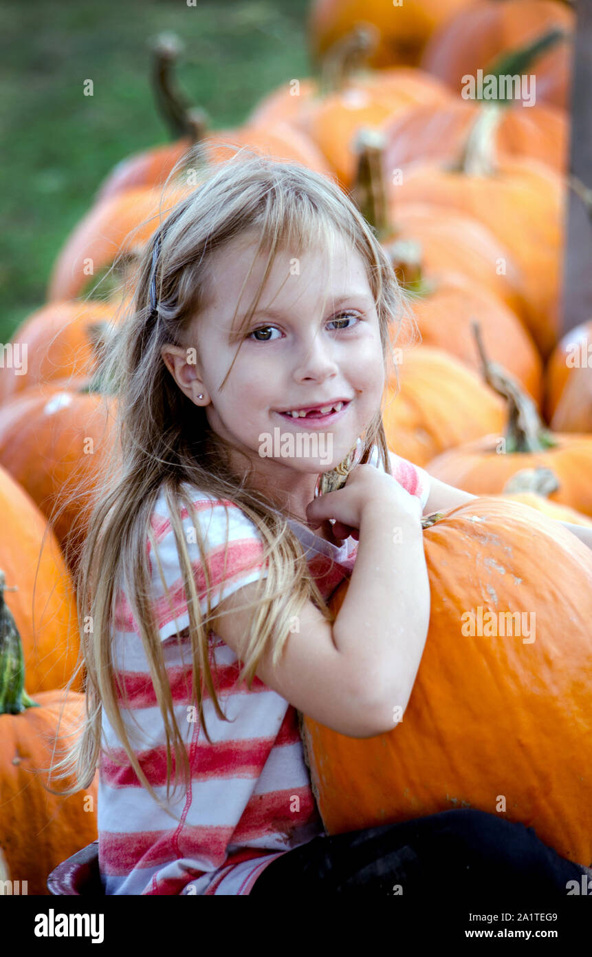 An adorable little blond girl chooses her favorite pumpkin from a busy Michigan USA pumpkin farm Stock Photo