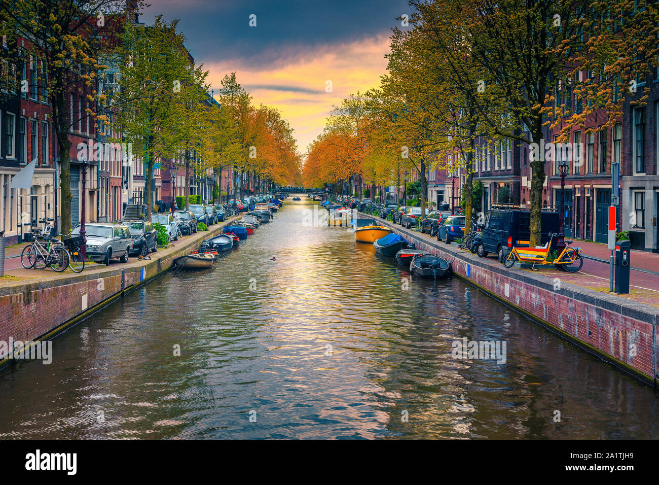 Stunning travel destination, narrow waterway and waterfront with traditional dutch houses. Colorful boats moored in water canal at sunset, Amsterdam, Stock Photo