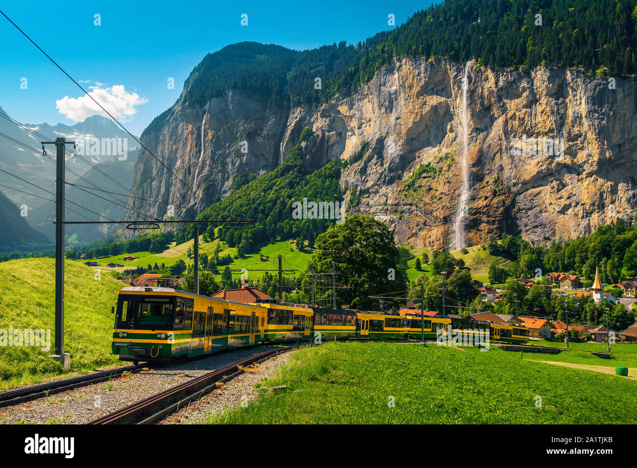 Unforgettable travel experience, modern electric tourist train and Lauterbrunnen village with high waterfalls in background, near Wengen village, Bern Stock Photo