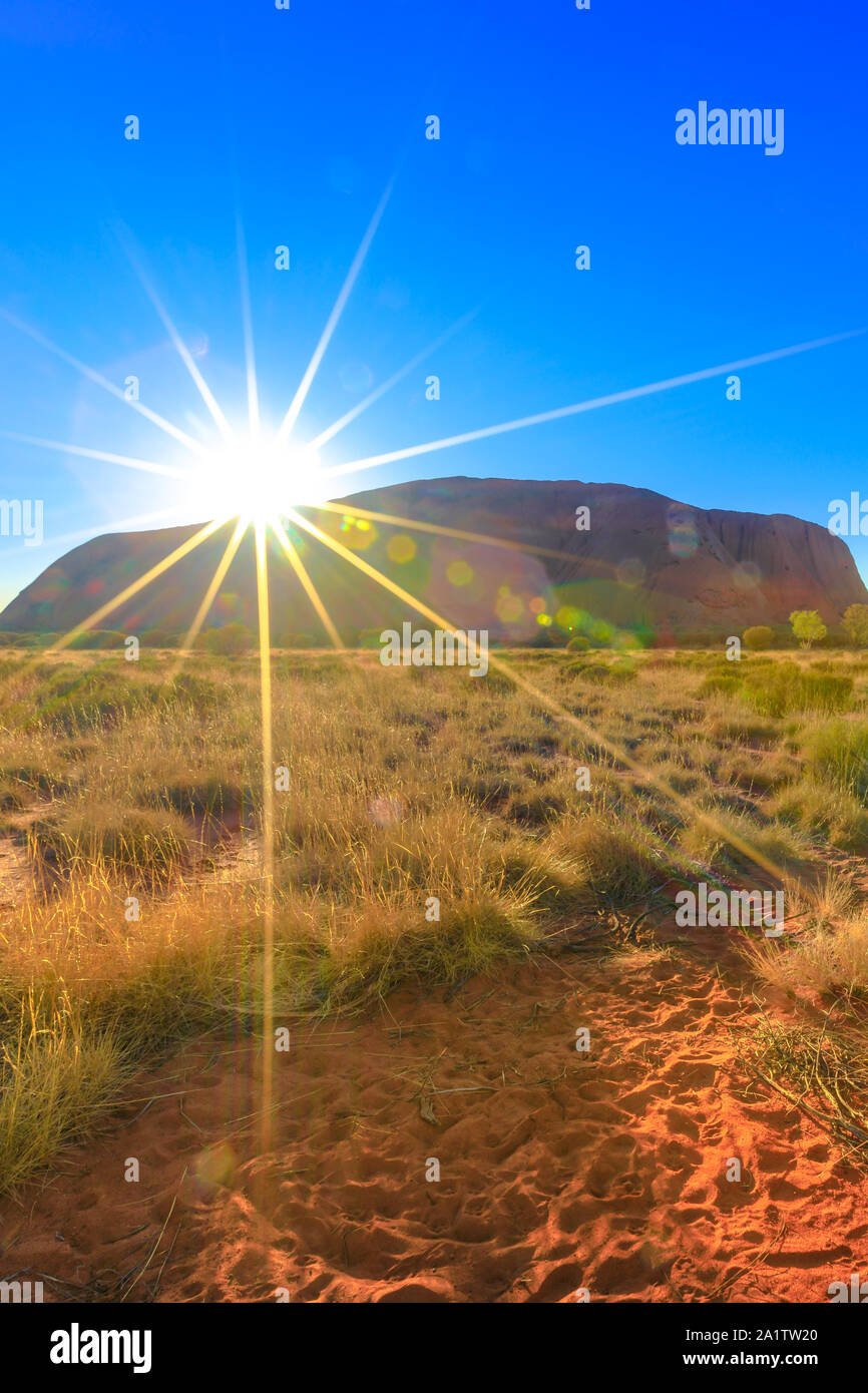 Sunbeams behind huge Ayers Rock at sunrise. Uluru illuminated by the rays of the early morning sun. Uluru-Kata Tjuta National Park, Australia Stock Photo