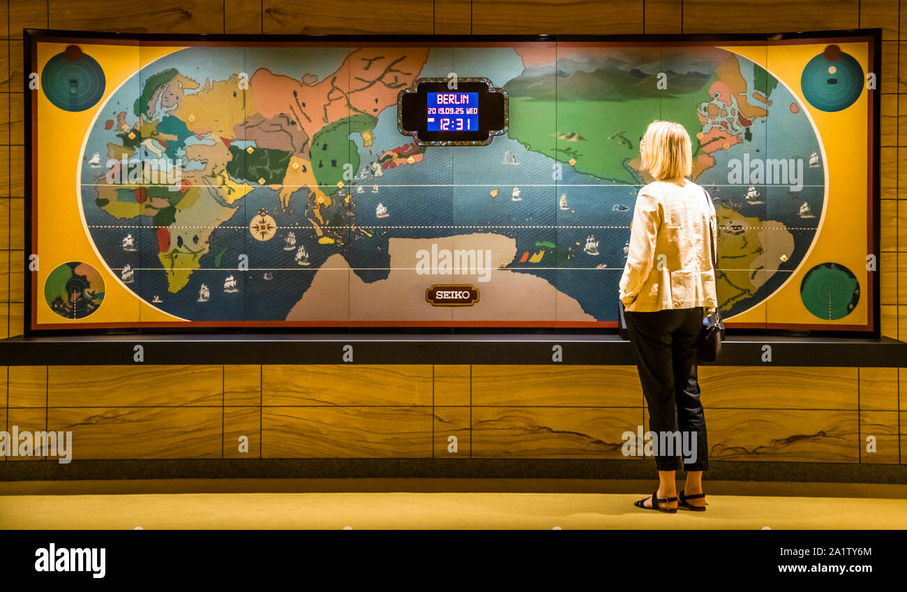 An interactive world clock at The Okura Tokyo, Minato ward, Japan, shows the time in Berlin at the push of a button: 2:31am, seven hours behind Tokyo. A visitor stands in front of the illuminated world map with ship symbols in the 1962 style. Built by Seiko, the restored clock comes from the old Hotel Okura, demolished in 2015, and is now part of the new lobby. Stock Photo