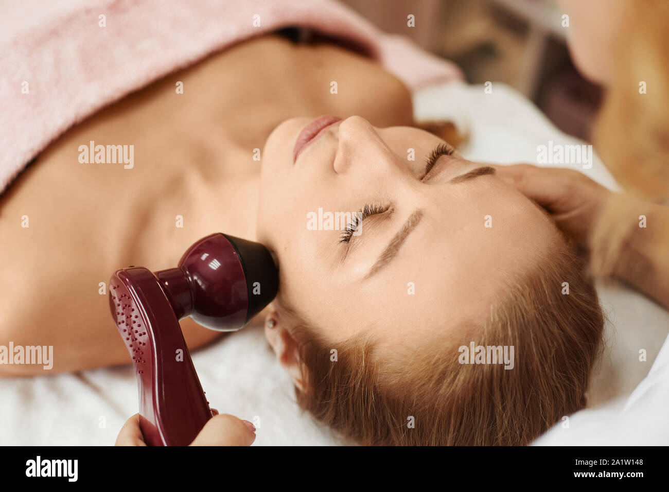 Beauty with perfect face skin on a non-surgical facelifting procedure. Woman receiving electric lift massage in spa salon. Electronic stimulation Stock Photo