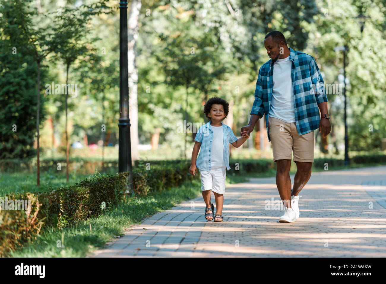 happy african american boy holding hands while walking with father ...