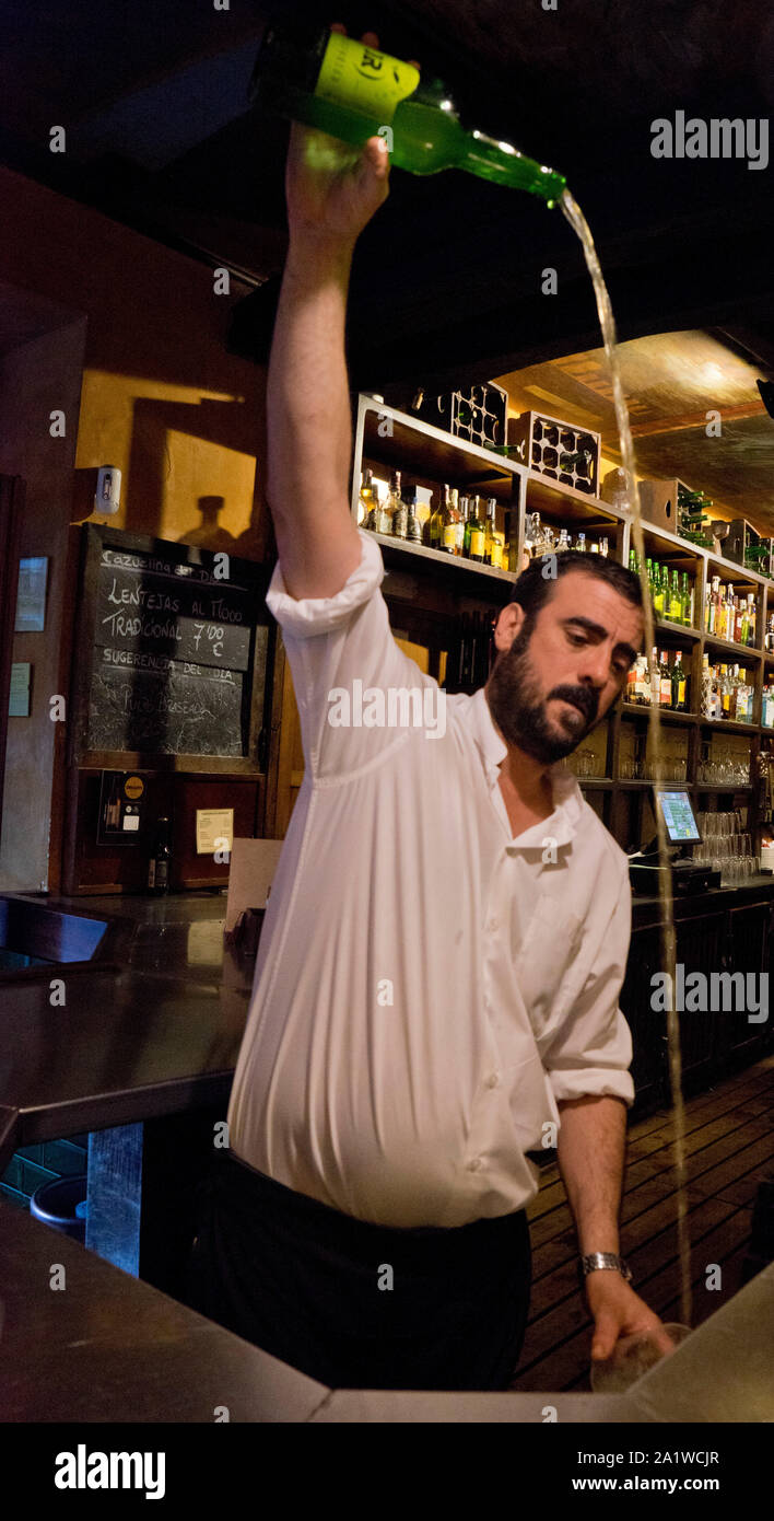Waiter pouring cider in the traditional Asturian way in a bar in Gijon