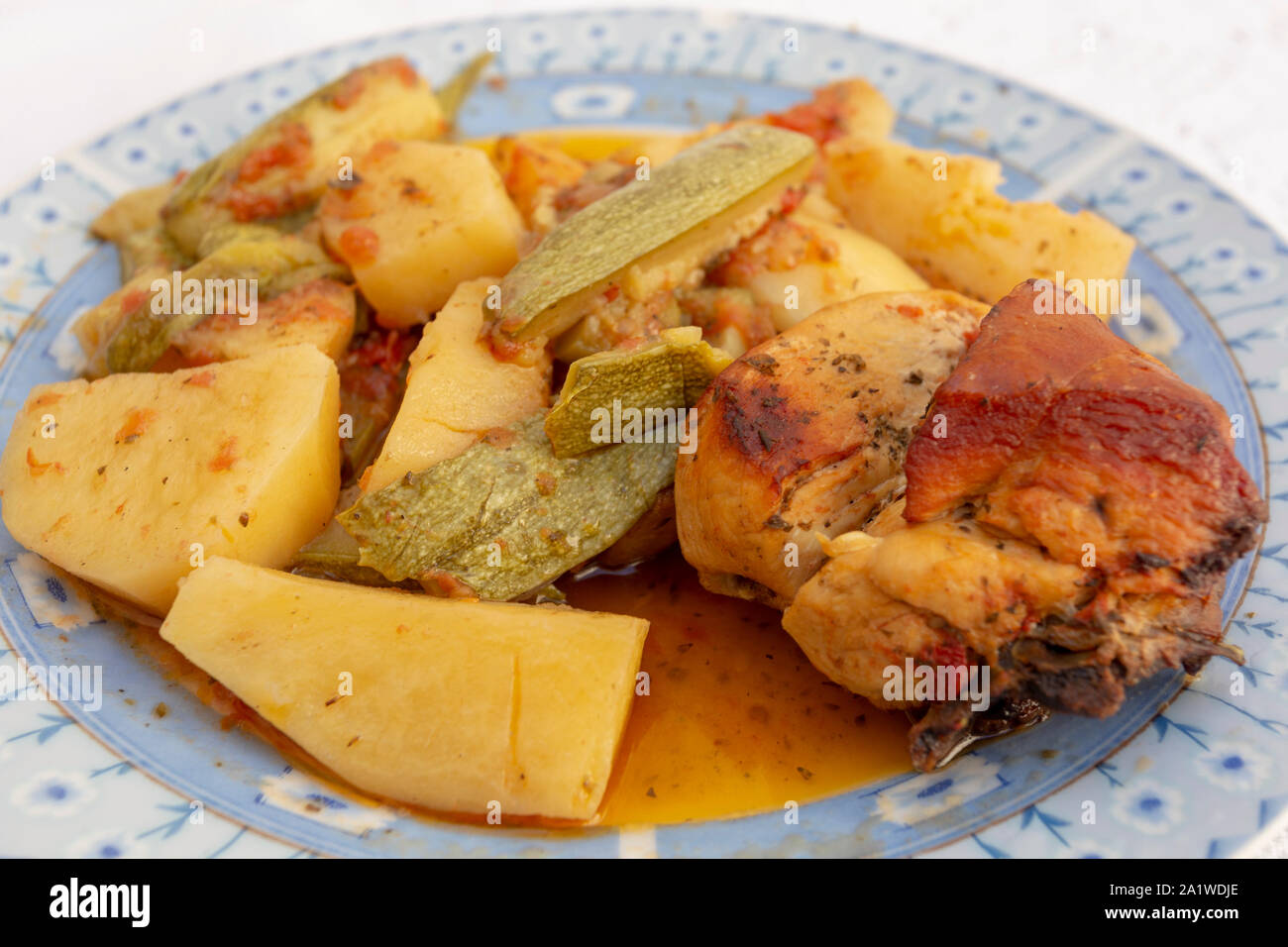 An authentic plate of Cretan oven-baked chicken with potatoes and courgettes (zuccini) in a rich tomato and herb olive-oil sauce Stock Photo