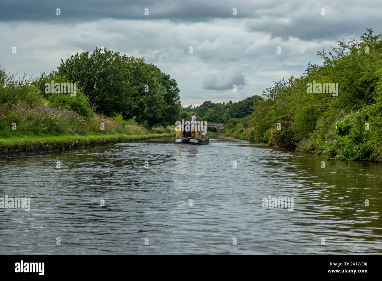 A man steering a Narrow Boat, or Barge,away from the photographer, on The Shropshire Union Canal in England. Stock Photo