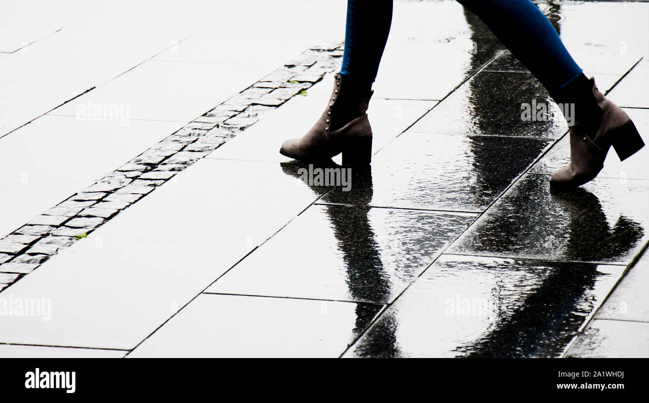 Silhouette shadow and reflection of a woman in  ankle boot shoes walking wet city street on a rainy day, legs only Stock Photo
