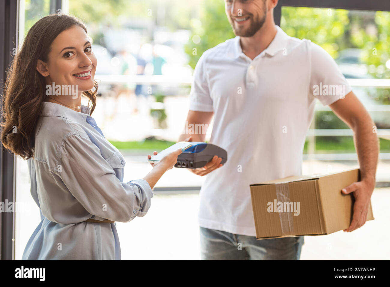 selective focus of happy woman paying while holding smartphone near credit card reader in hand on delivery man Stock Photo