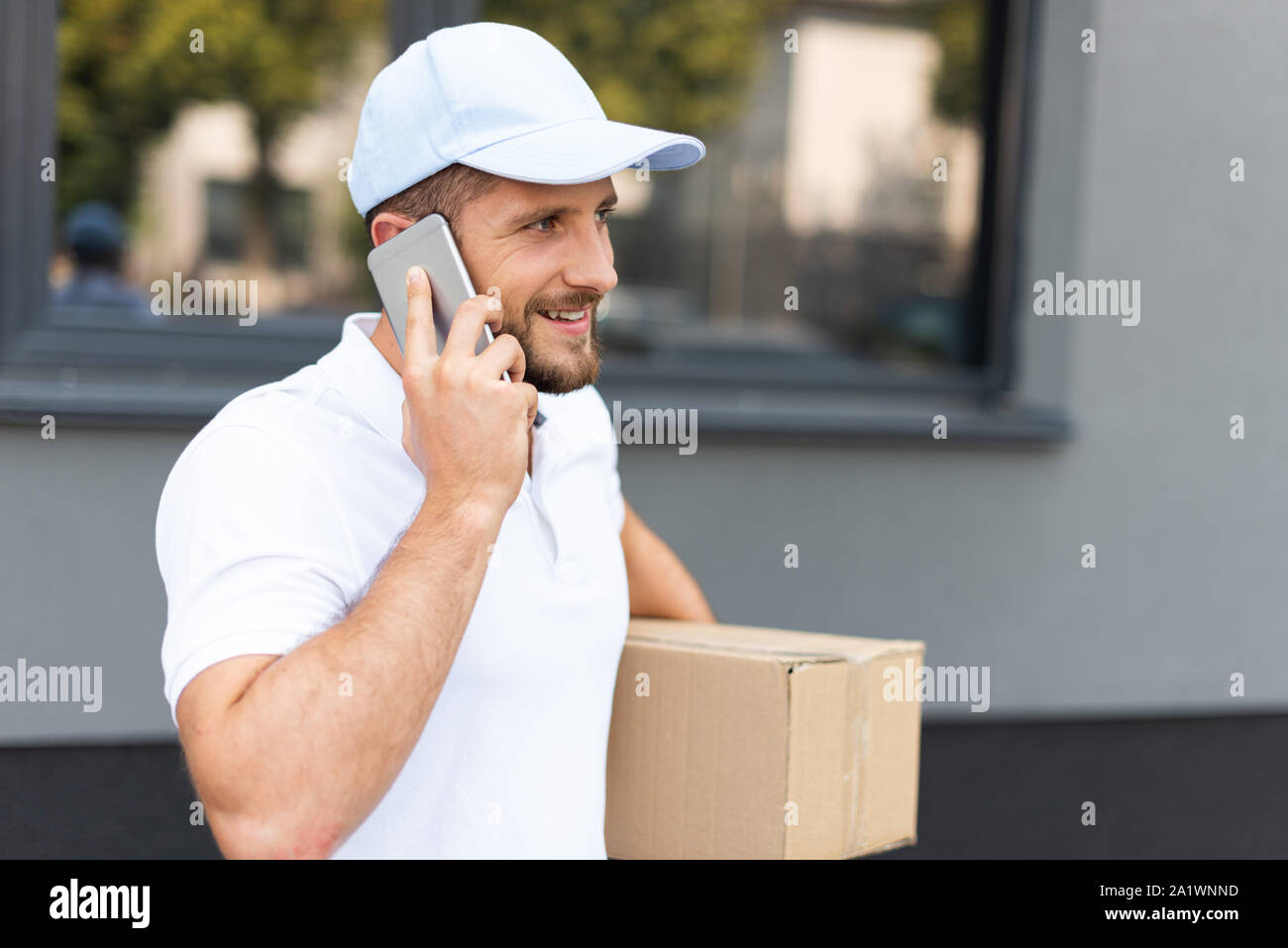 happy bearded delivery man talking on smartphone while holding box Stock Photo