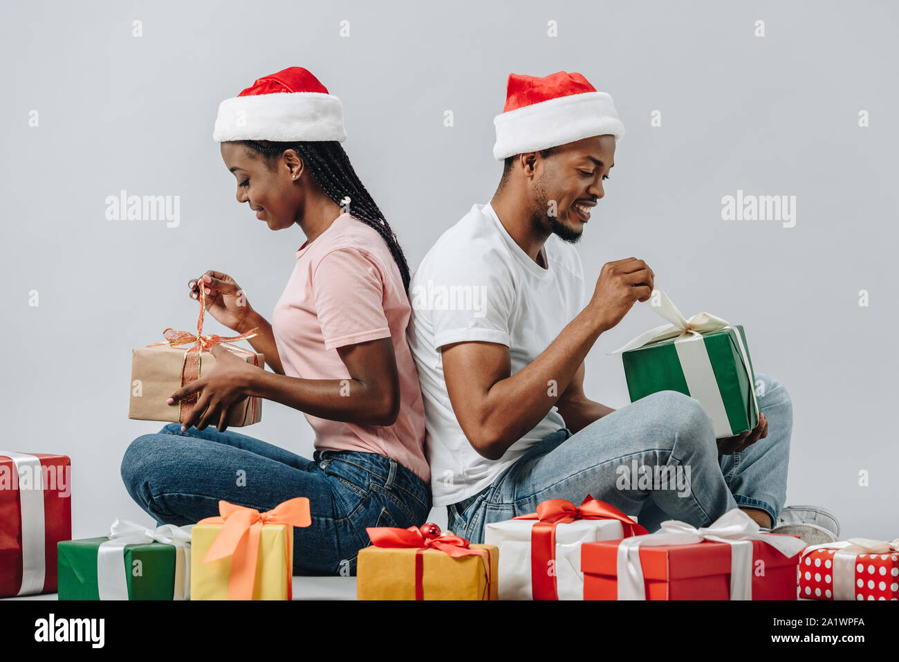 African American couple in Santa hat sitting back to back and opening ...
