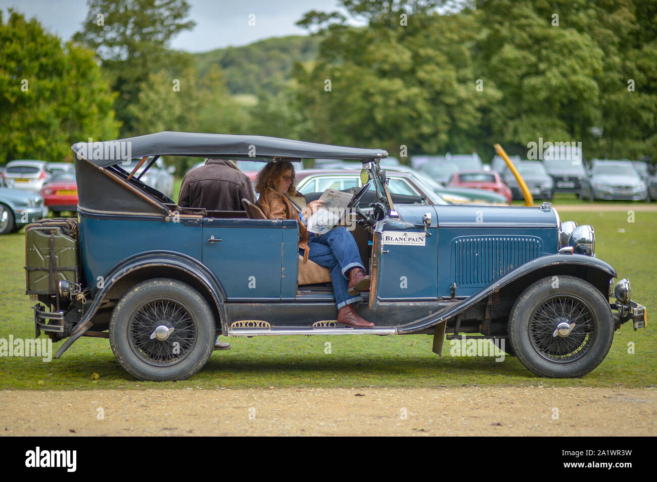A woman reads a newspaper in an old Chrysler at a classic car gathering at Sudeley Castle, Cotswolds, where several classic car owners have braved the weather to show their vehicles. Stock Photo