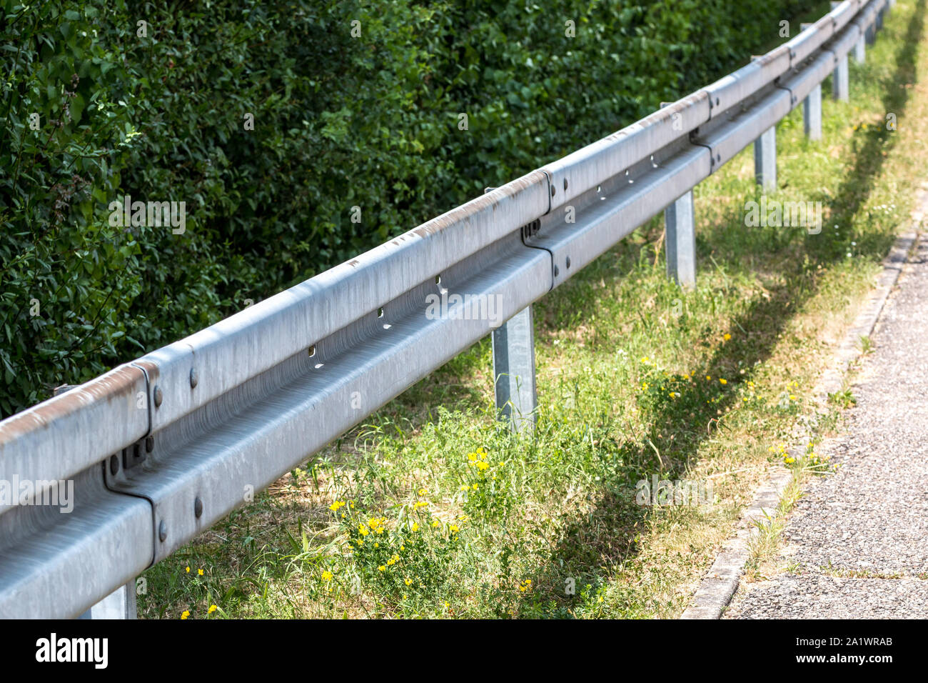 Crash barrier by the street with bushes, grass and asphalt Stock Photo