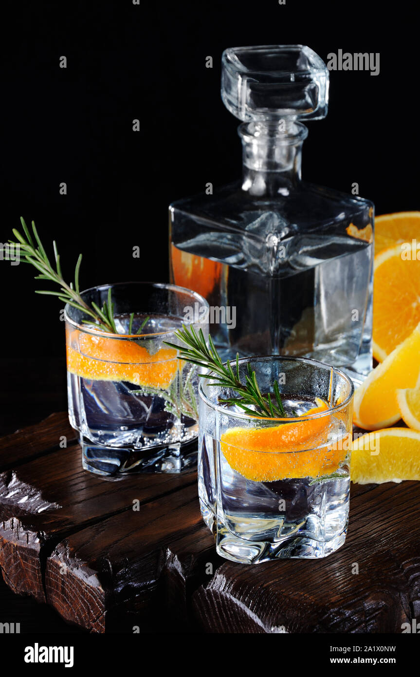 Cocktail classic Dry Gin with tonic and orange zest with a sprig of rosemary on a wooden board with  slices   juicy orange Stock Photo