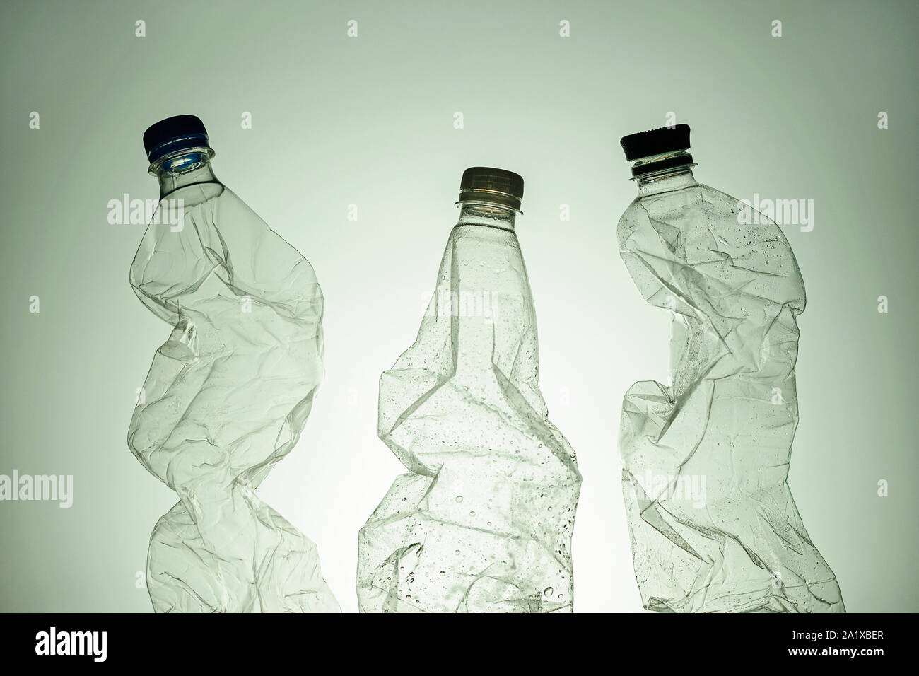 Three empty clear wet plastic bottles for recycling over a green background in a conceptual image Stock Photo