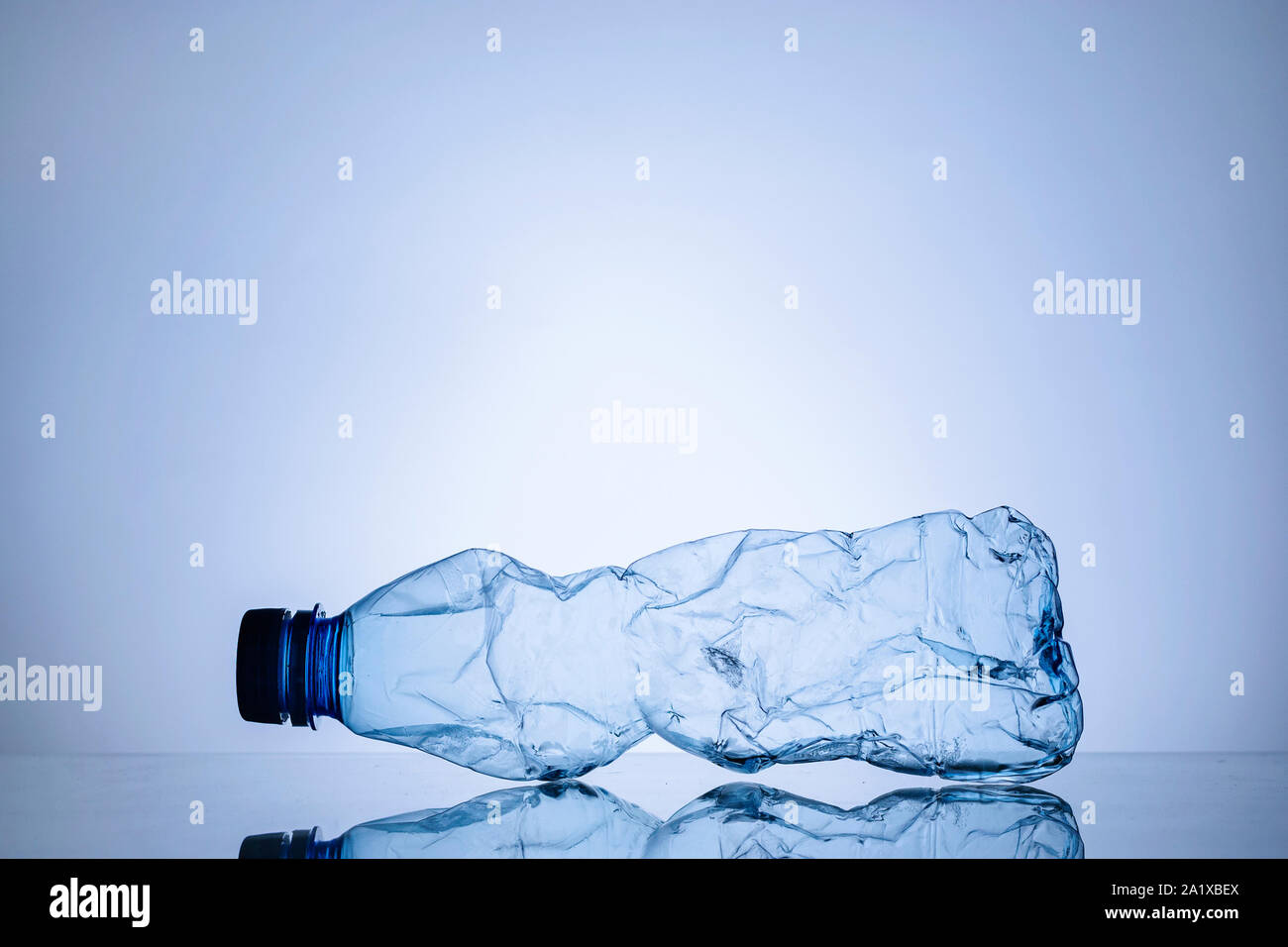 Crumpled empty clear plastic bottle on blue background with reflection i a concept of plastic waste and pollution with copy space Stock Photo