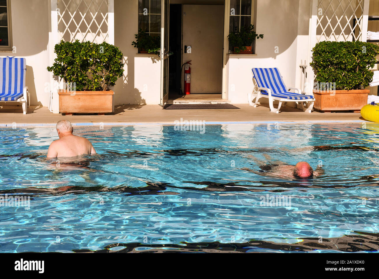 Two senior men from behind swimming in the pool of a hotel in a sunny summer day, Lido di Camaiore, Versilia, Tuscany, Italy Stock Photo