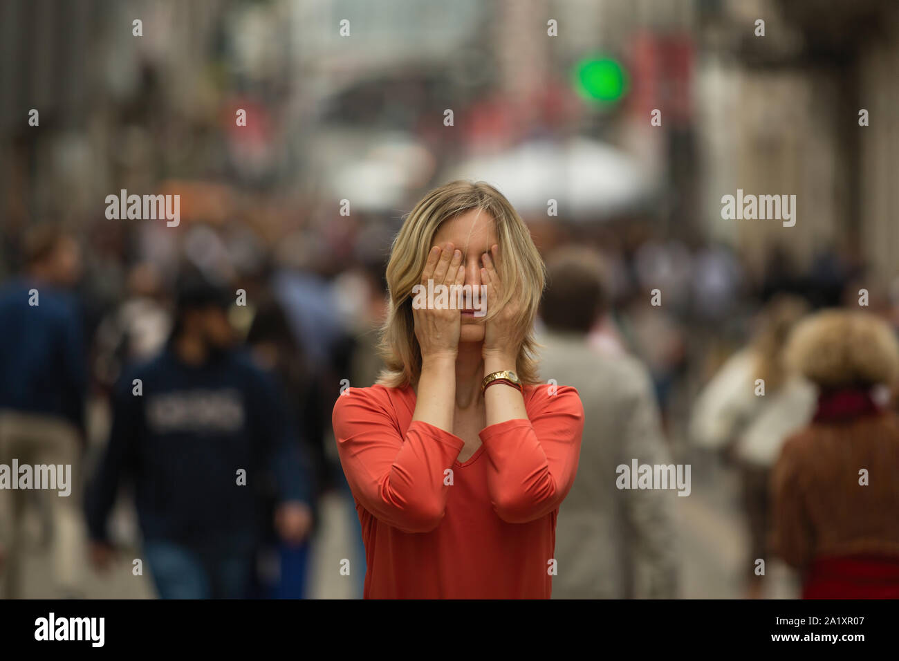 Young depressed woman covers his eyes with his hands at standing in the middle of a crowded street. Stock Photo