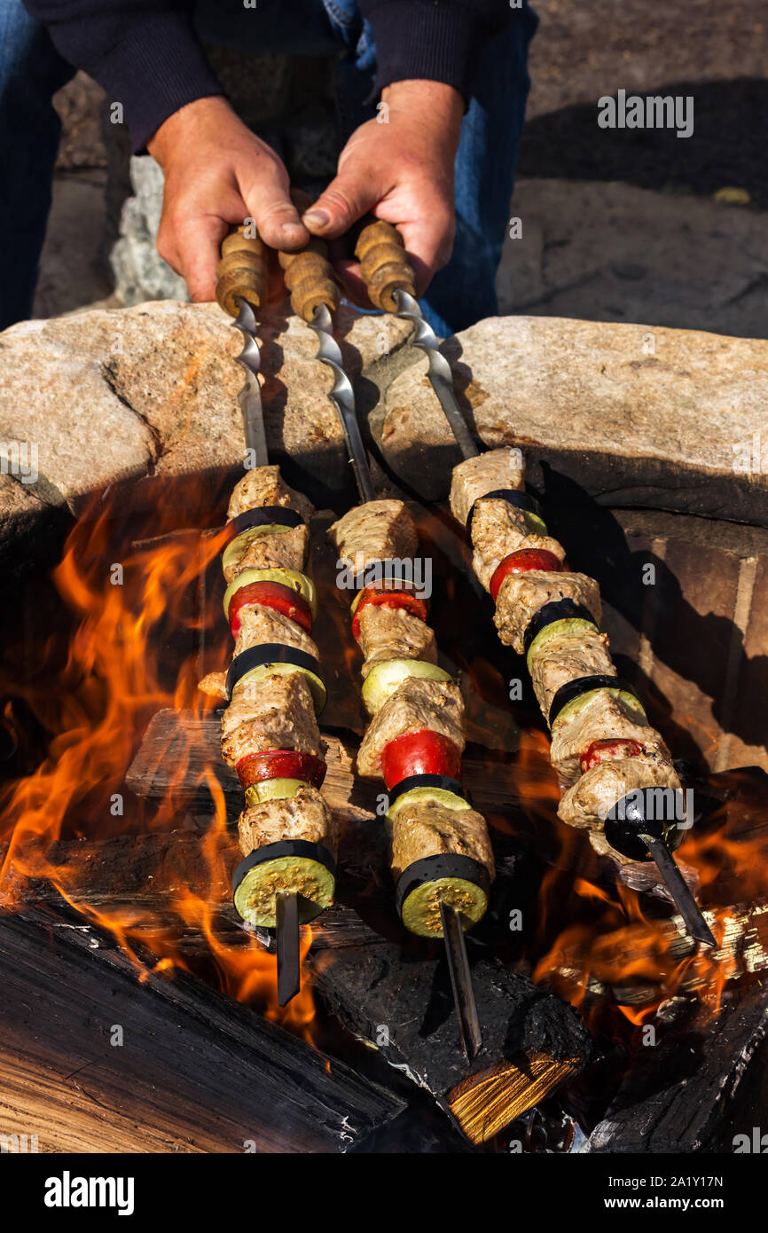 Men's hands hold three kebabs with vegetables over a fire. View from above Stock Photo