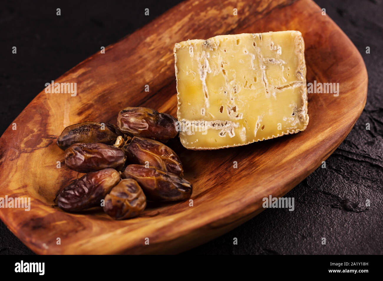 piece of old blue cheese and a branch of dates  lie on a wooden dish. View from above Stock Photo