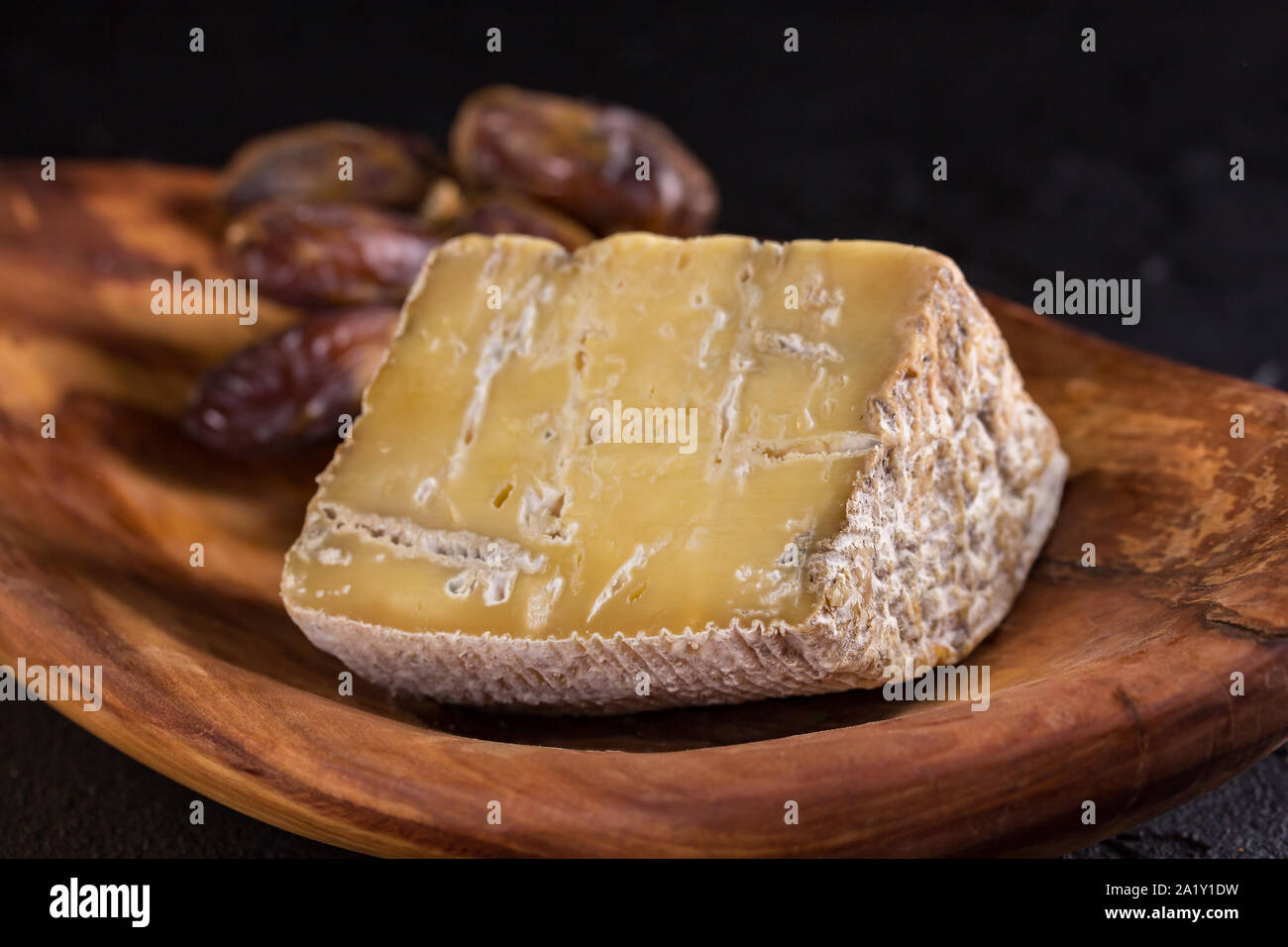 piece of old blue cheese and a branch of dates  lie on a wooden dish Stock Photo