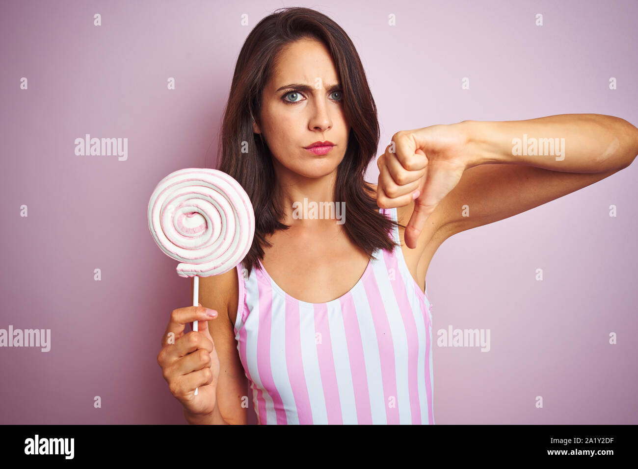 Young beautiful woman eating sweet candy over pink isolated background ...