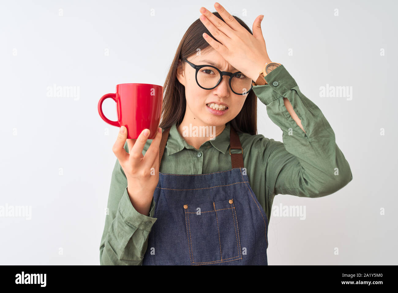 Chinese barista woman wearing apron glasses drinking coffee over isolated white background stressed with hand on head, shocked with shame and surprise Stock Photo