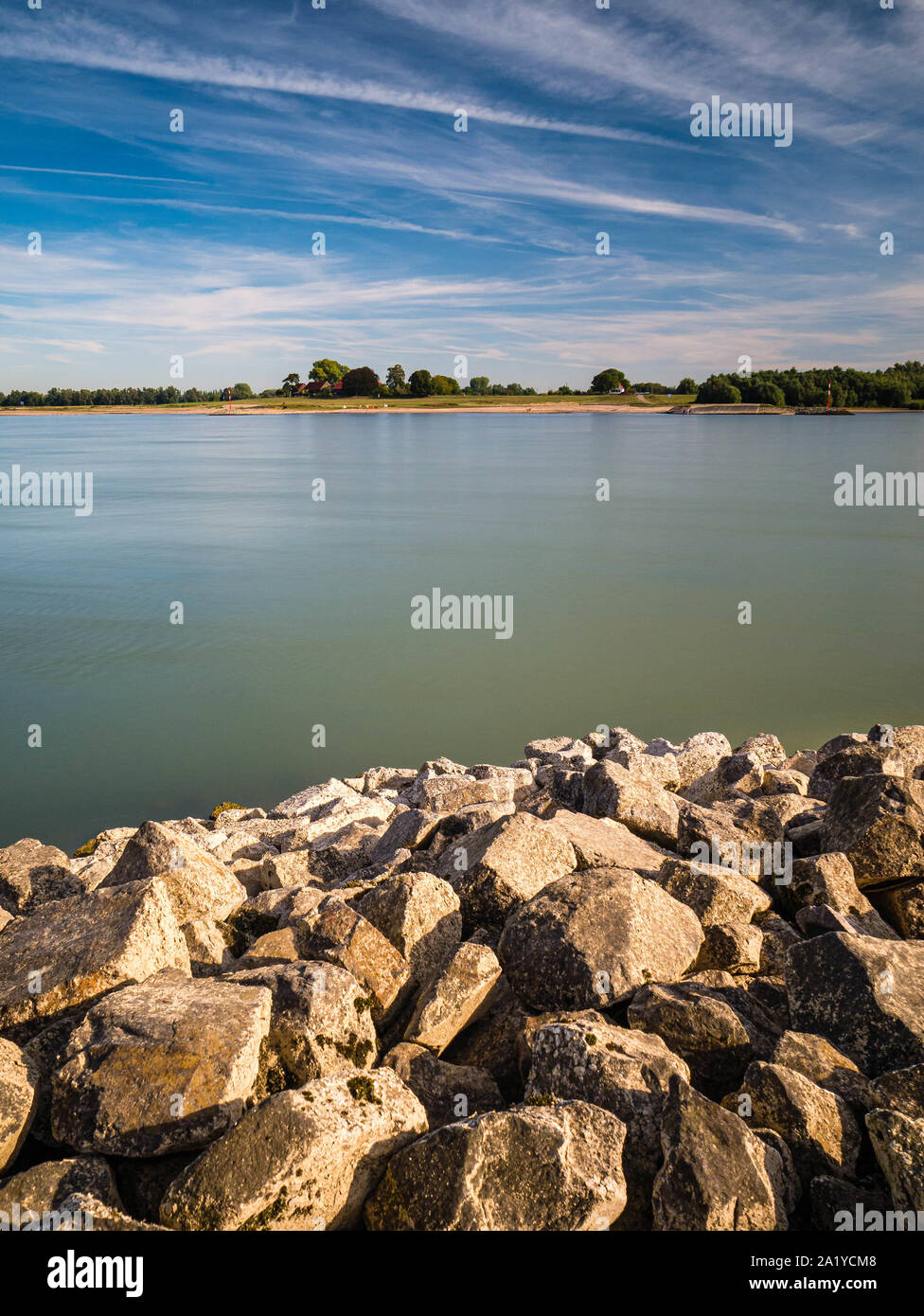 Calm rhine river with rocky bank in the foregound and sandy beach in the distance Stock Photo