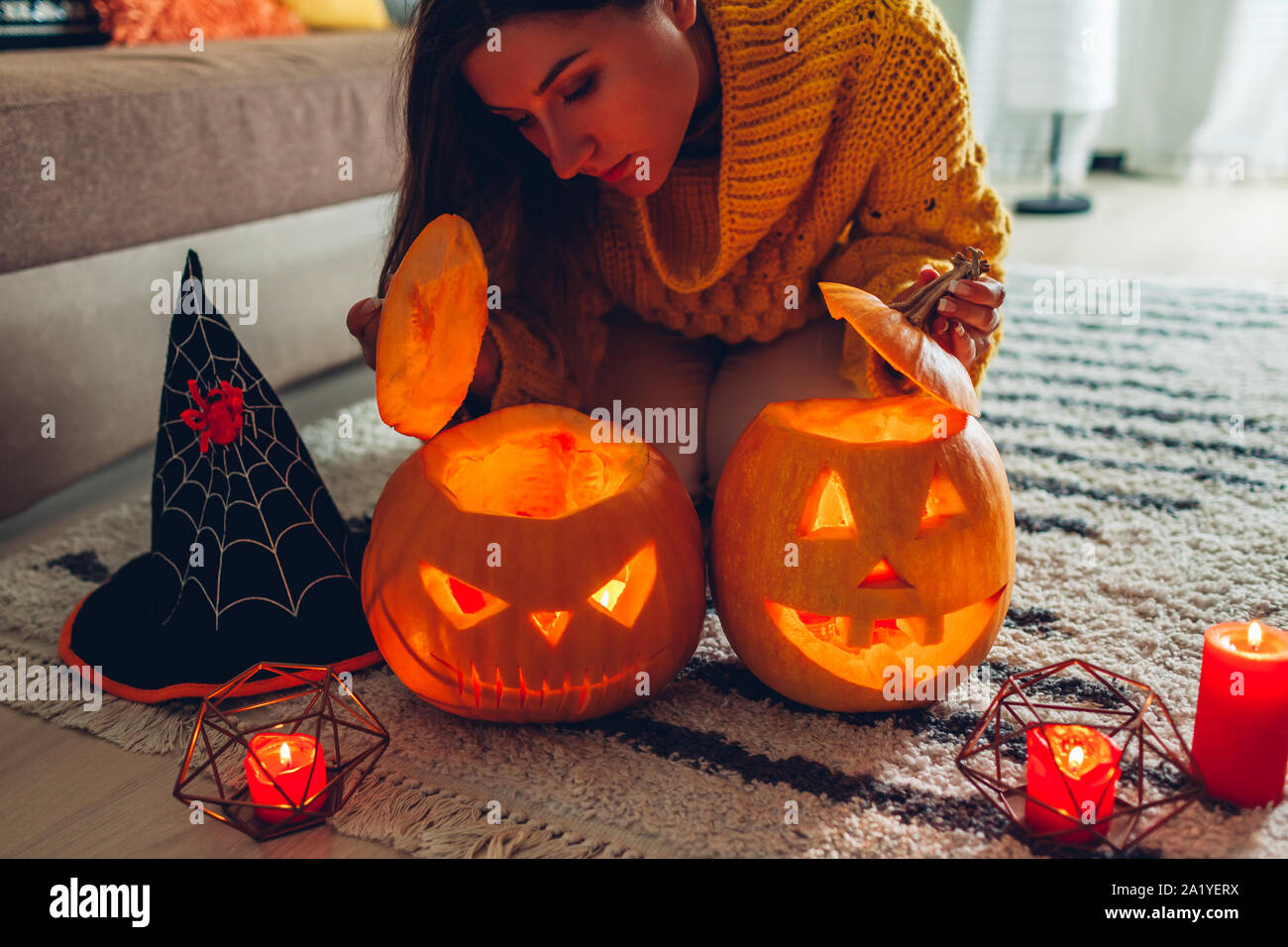 Halloween jack-o-lantern pumpkins. Woman opens pumpkins and looks inside at home. Mysterious holiday Stock Photo