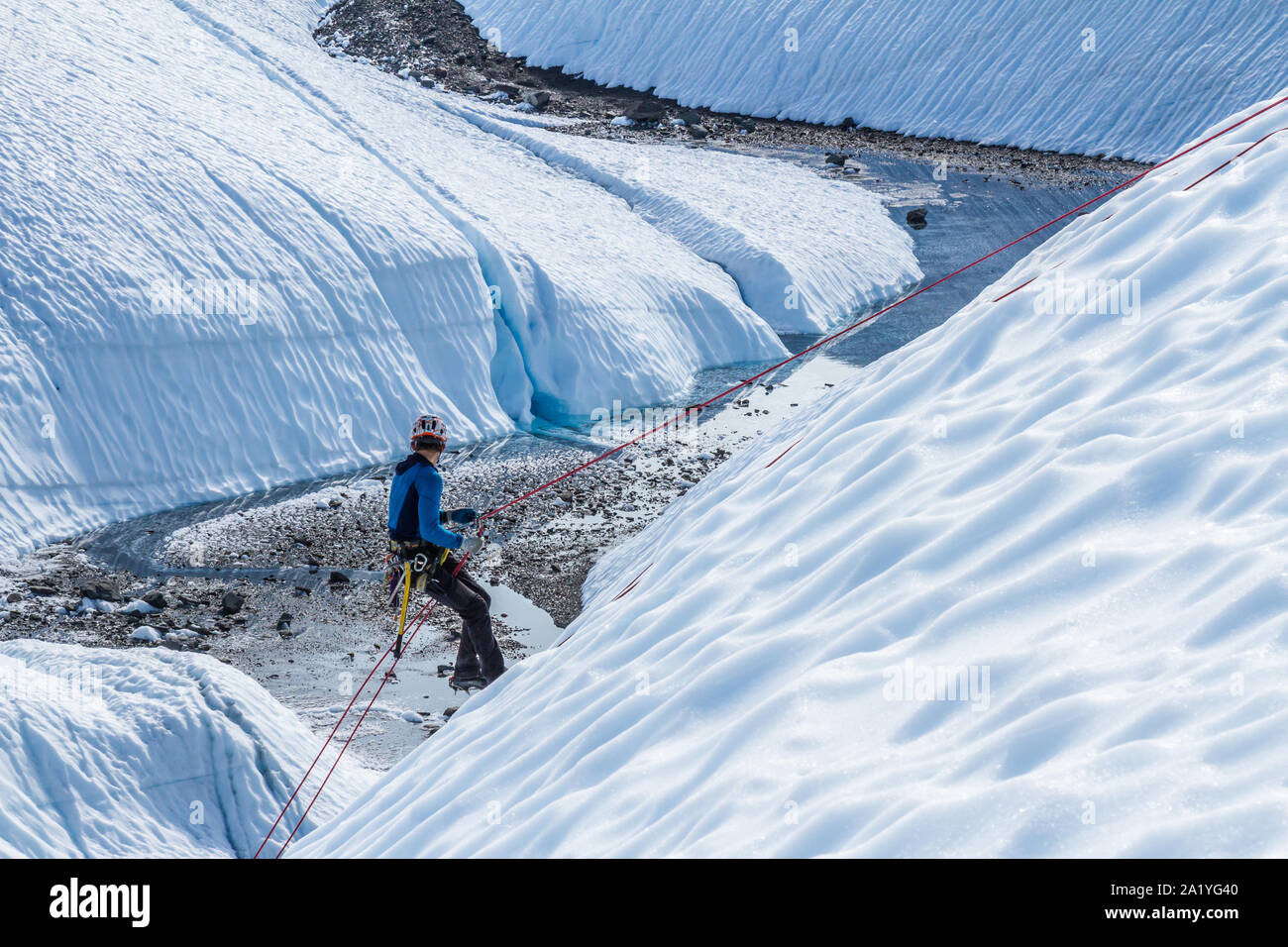 A Young Man Rappels Or Abseils Down A Rope On A Steep Ice Slope On The