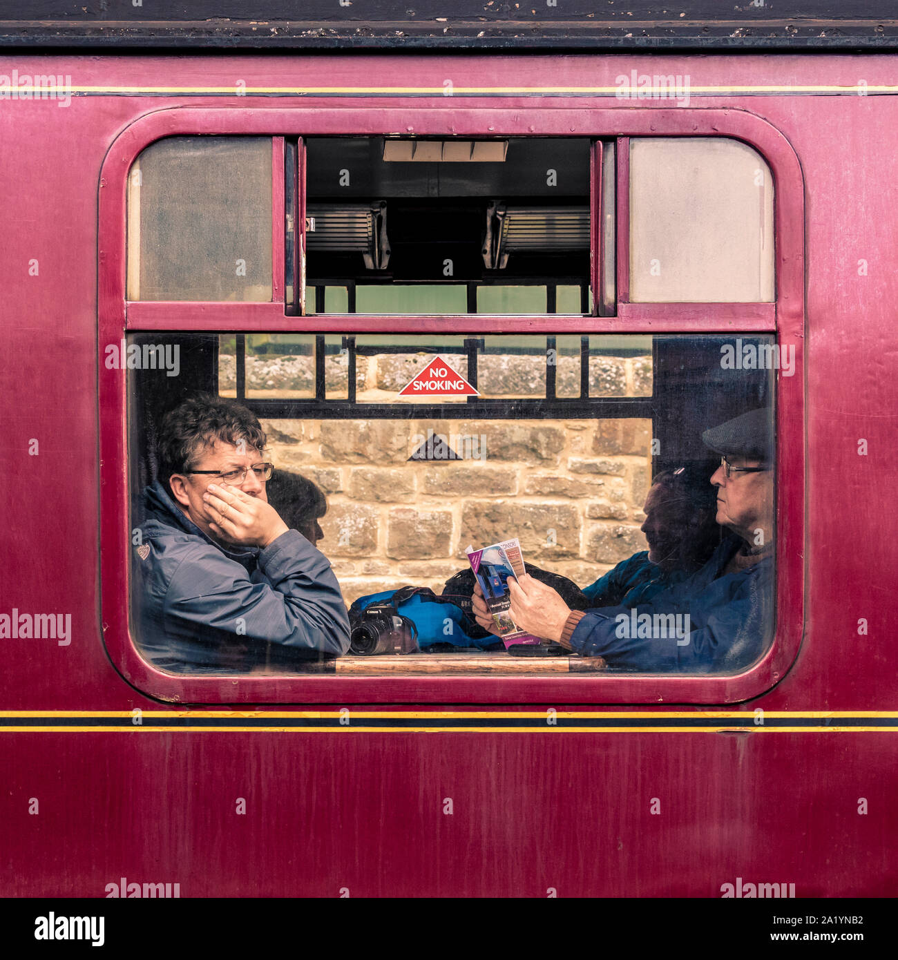 Passengers framed in the window of a vintage train carriage on the North Yorkshire Moors Railway, waiting to depart. UK Stock Photo