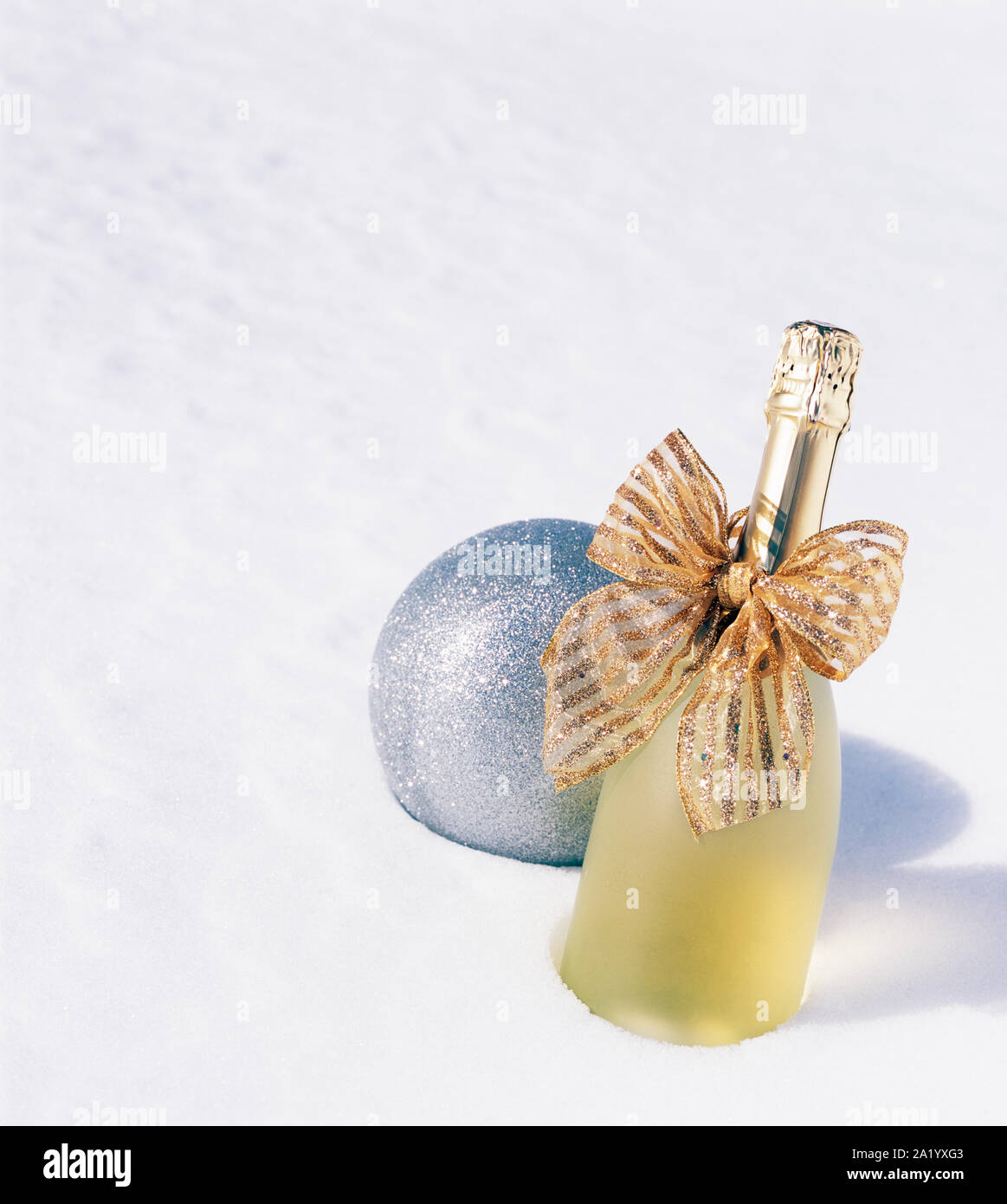 Bottle of Champagne sparkling wine with gold ribbon bow and glitter ornament on white snow background. Festive Christmas and New Year's Eve drinks. Stock Photo