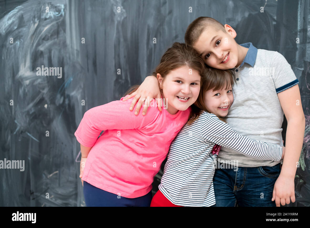 group portrait of happy kids hugging each other while having fun in front of black chalkboard Stock Photo